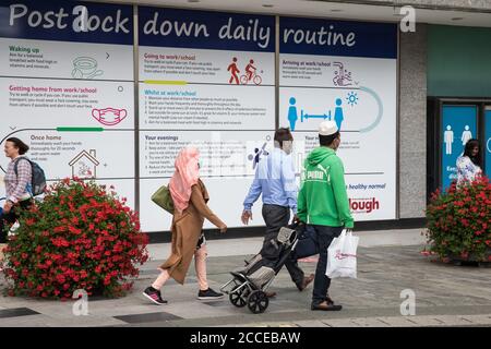 Slough, Regno Unito. 21 agosto 2020. I membri del pubblico che indossano copriviso passano davanti alle esposizioni di informazioni pubbliche COVID-19 nel centro della città. Slough è stata elencata dal Public Health England (PHE) e dal Department of Health and Social Care (DHSC) come ‘area di preoccupazione’ per COVID-19 a seguito di un aumento dei casi positivi di coronavirus nelle ultime due settimane. Credit: Mark Kerrison/Alamy Live News Foto Stock