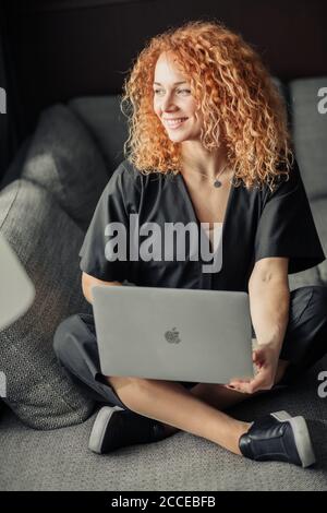 Felice sorridente imprenditore donna decapitato in azienda di startup che lavora al portatile comodamente seduto al divano. Foto Stock