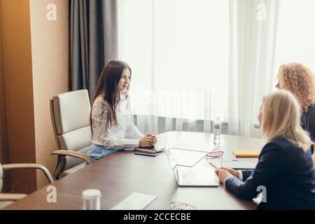 Tre giovani donne caucasiche di affari focalizzate con i capelli differenti che lavorano insieme, brainstorming in ufficio. Foto Stock