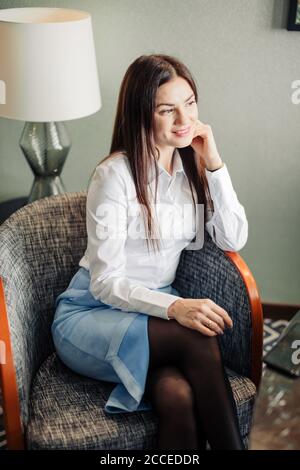 Foto di una donna affascinante dai capelli castani sorridente seduta su una poltrona in camera d'albergo Foto Stock