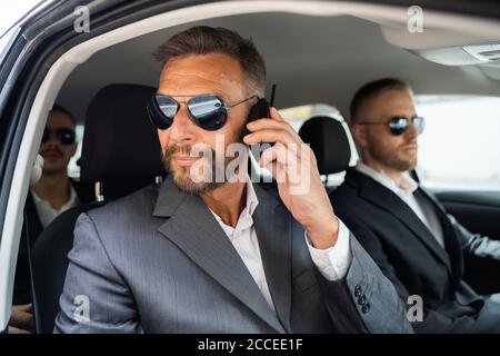 Guardia di sicurezza in occhiali da sole all'interno dell'auto che parla su Walkie Talkie Foto Stock