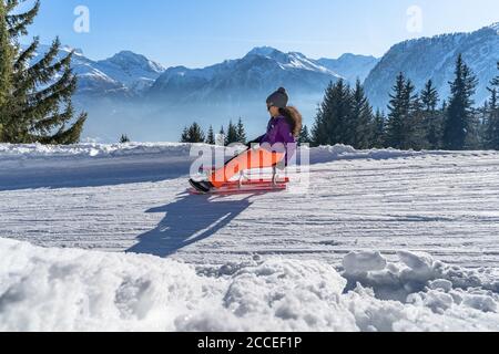 Europa, Svizzera, Vallese, Belalp, giovane donna che slitta sullo sfondo delle Alpi Vallesi Foto Stock