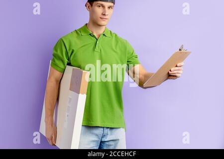 ritratto di giovane uomo caucasico di consegna in t-shirt verde, bel contenitore pizzaman con pizza e lista di set di pizza ordinati. corriere, consegna Foto Stock