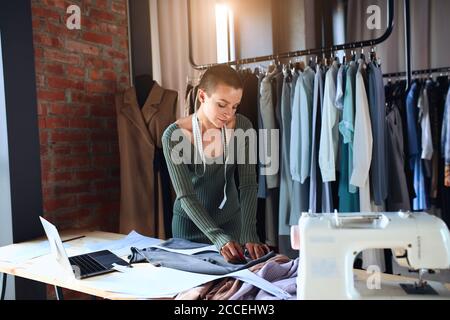 Il sarto caucasico segna con attenzione sugli abiti. Creazione di un nuovo abito in studio di design Foto Stock