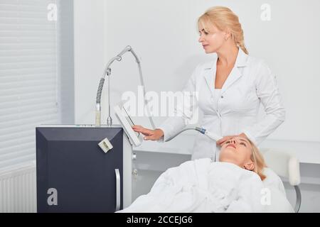 attraente strumento di preparazione per la pulizia del viso del paziente. primo piano foto, terapeuta che tocca lo schermo dell'apparecchiatura prima del trattamento Foto Stock