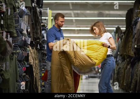 giovane coppia scompattata sacco a pelo per campeggio in negozio di abbigliamento sportivo, scelgono il più caldo e confortevole, nella navata con assortimento Foto Stock