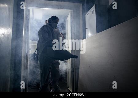 Disinfettante professionale in un dispositivo di protezione personale NBC tuta ppe, guanti, maschera, pulizia di spazi isolati con disinfettante spray pressurizzato w Foto Stock