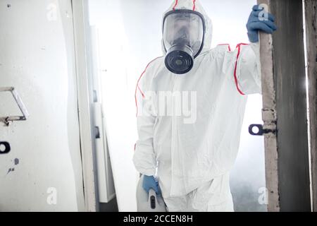 Disinfettante professionale in un dispositivo di protezione personale NBC tuta ppe, guanti, maschera, pulizia di spazi isolati con disinfettante spray pressurizzato w Foto Stock