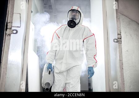 Disinfettante professionale in un dispositivo di protezione personale NBC tuta ppe, guanti, maschera, pulizia di spazi isolati con disinfettante spray pressurizzato w Foto Stock