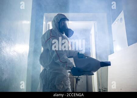 Pandemia mondiale COVID-19. Disinfettante professionale in tuta protettiva interna, uccidere e rimuovere i batteri dalle superfici in spazio isolato. Coronavirus c Foto Stock