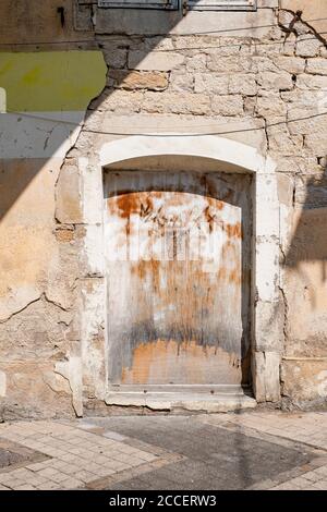 Porta in legno intemperie con graffiti su una facciata in pietra naturale con intonaco sgretolante Foto Stock