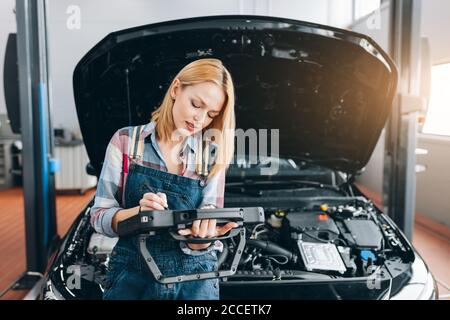 Bella bionda ragazza si è concentrata sul lavoro con il PC tablet digitale presso il negozio di riparazione. Primo piano foto. Copia spazio. Diagnostica rapida Foto Stock