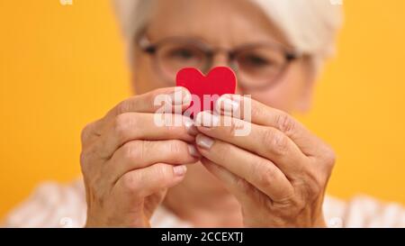 Primo piano. Donna anziana felice che mostra la forma del cuore tra le dita. Amore emozione e concetto di sostegno. Foto di alta qualità Foto Stock