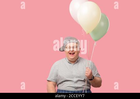 Divertente adorabile animatore tubby, uomo del mini club, con emozioni vivide che guardano allegro, sorridente felicemente, in posa alla telecamera, tenendo palloncini d'aria isola Foto Stock