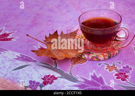 tazza di tè e foglia d'arancia seduta sul tavolo esterno su tovaglie colorate Foto Stock