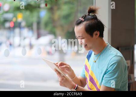 Primo piano un giovane asiatico sorridente, utilizzando un computer tablet al chiuso Foto Stock