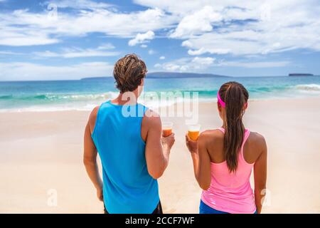 Persone sane stile di vita attivo. I corridori del fitness si accoppiano sulla spiaggia bevendo il succo di frutta della prima colazione in tazze di frullato guardando l'oceano. Sfondo estivo Foto Stock