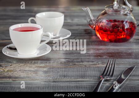 Teiera rosa bacche rossa, tazze bianche, posate su sfondo grigio di legno Foto Stock