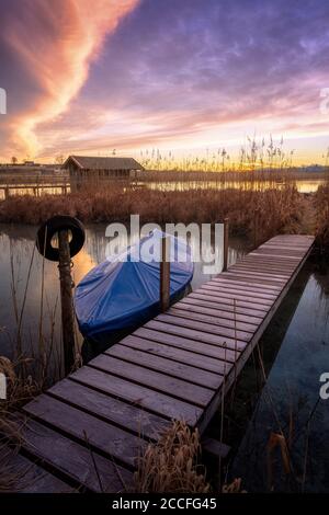 Molo e barca sulla riva del lago all'alba Foto Stock