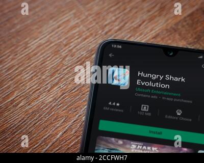 LOD, Israele - 8 luglio 2020: App Hungry Shark Evolution play store page sul display di uno smartphone nero su sfondo di legno. Vista dall'alto piatta Foto Stock