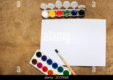 Set di vernici ad acquerello, pennelli per pittura e foglio bianco vuoto di carta di schizzo. Foto Stock