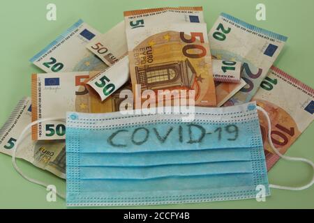 I lotti sulle banconote in euro coprono con maschera protettiva facciale con Testo COVID-19 primo piano Foto Stock