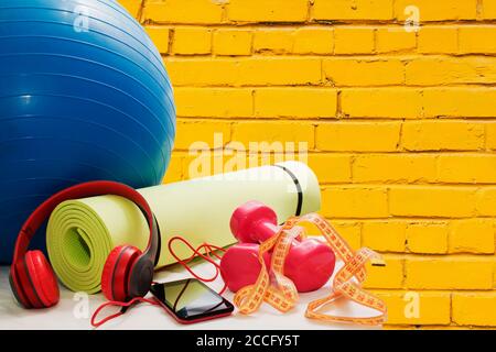 Manubri, tappetino, smartphone e auricolari su sfondo giallo in mattoni Foto Stock