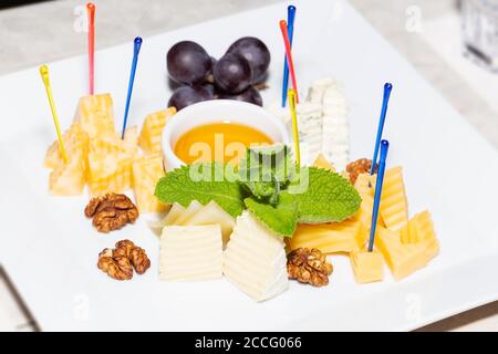 Piatto di formaggi servito con uva, noci e miele primo piano. Foto Stock