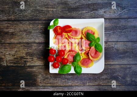 Pasta fatta in casa / ravioli ripieni di barbabietola su un piatto bianco con fondo tavola in legno. Pomodori e basilico fresco per la decorazione. Foto Stock