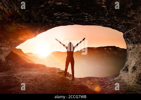 La silhouette di una donna saluta l'alba in una grotta Foto Stock