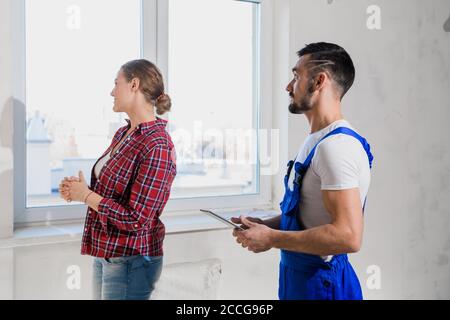 Un operaio in uniforme blu mostra alla cliente femminile il rinnovo di un appartamento. Scrive note Foto Stock