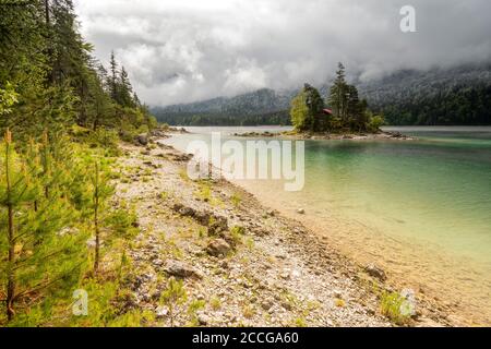 Piccola isola solitaria con cabina in legno e tetto rosso, nel bel mezzo dell'Eibsee sotto lo Zugspitze nelle Alpi bavaresi del Wetterstein Foto Stock