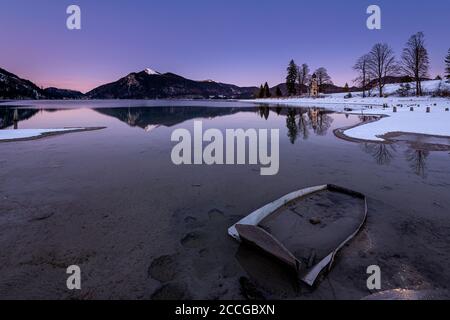 Una vecchia barca da pesca nel fango sulle rive del lago di Walchen sulla penisola di Zwergern. Sullo sfondo il lago di verricello, la cappella di San Margareth e. Foto Stock