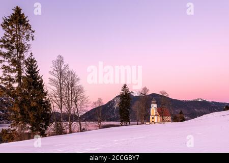 La piccola cappella di San Margareth am Walchensee nel bagliore serale. Sullo sfondo il Walchensee e Jochberg in inverno Foto Stock