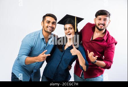 Bella giovane studentessa indiana laureata che celebra il successo con il maschio Amico mentre indossa il cappello della cerimonia di laurea su sfondo bianco Foto Stock