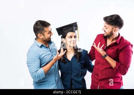 Bella giovane studentessa indiana laureata che celebra il successo con il maschio Amico mentre indossa il cappello della cerimonia di laurea su sfondo bianco Foto Stock