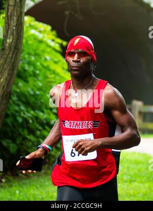 Babylon, New York, USA - 12 agosto 2018: Un corridore afroamericano con bandana rossa con il flash sidn su di esso durante la gara di pista sporca calzino 10K. Foto Stock