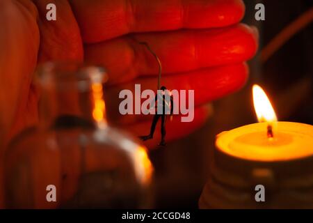 Concetto - giocare con il fuoco / attività rischiosa / pericolo - mano a cupola che tiene una figura in miniatura da un filo vicino alla candela che brucia Foto Stock