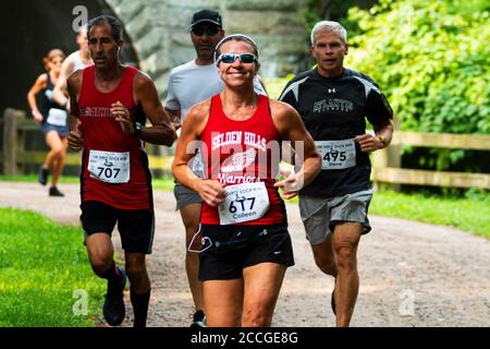 Babylon, New York, USA - 12 Agosto 2018: Donne sorridenti mentre corrono la gara di pista sporca calza 10K. Nel bosco dopo essere uscito dal tunnel. Foto Stock