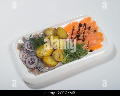 Affettato pesce rosso salato, aringhe, patate bollite, cipolle, verdi su un piatto. Antipasto freddo. Banchetti, menu a buffet Foto Stock