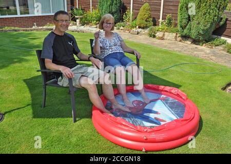 Rinfrescarsi in coppia sul prato con i piedi nella piscina per bambini durante l'incantesimo caldo Foto Stock