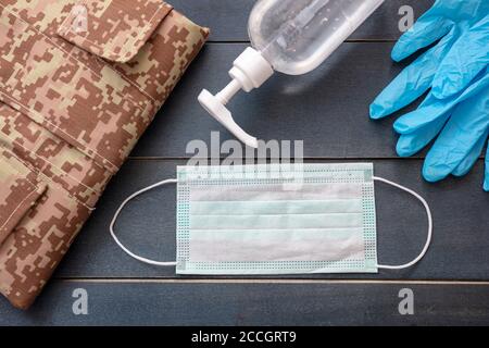 Concetto di protezione del coronavirus dell'esercito. Disinfettante per le mani, guanti protettivi, maschera medica e uniforme dell'esercito statunitense su sfondo di legno di colore blu. Covid Foto Stock