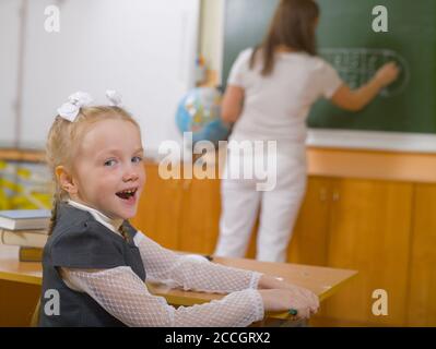 La studentessa è seduta alla scrivania, tornando indietro. L'insegnante scrive sulla lavagna in background Foto Stock