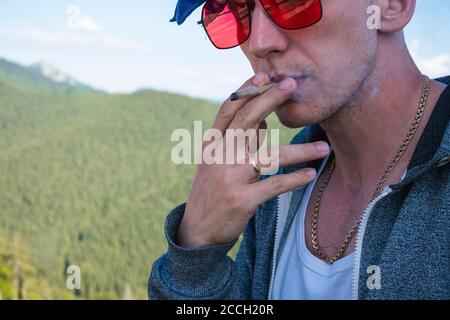 Primo piano di un giovane uomo che fuma marijuana comune all'aperto. Canapa smussata nella mano maschio. La cannabis è un concetto di erbe e medicina alternativa Foto Stock