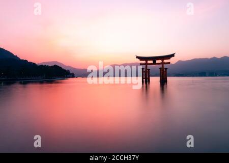 Il sole tramonta dietro la porta dei tori galleggiante al Santuario di Istukushima a Miyajima, Hiroshima, Giappone Foto Stock