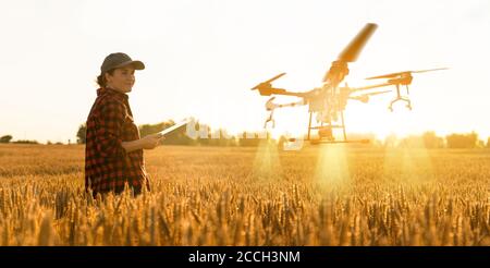 Donna contadina controlla il drone con una tavoletta. Agricoltura intelligente e agricoltura di precisione Foto Stock