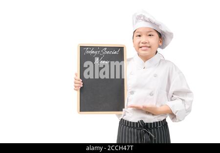 Happy chef ragazza asiatica in uniforme che presenta il menu speciale di oggi su lavagna isolata su sfondo bianco, per l'inserimento di testo o menu con spazio di copia Foto Stock