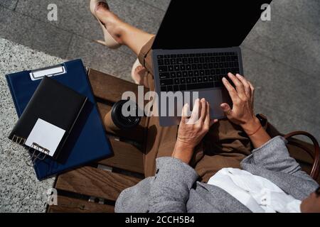 Business online. Vista dall'alto di una donna d'affari seduta sulla panca all'aperto e che utilizza su un computer portatile, lavorando online e bevendo caffè Foto Stock