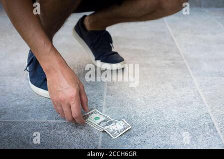 Uomo anonimo, vestito casual, con sneakers blu, raccogliendo un conto del dollaro dal suolo. Foto Stock