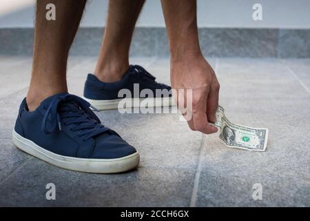 Uomo anonimo, vestito casual, con sneakers blu, raccogliendo un conto del dollaro dal pavimento. Foto Stock
